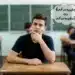 Estudante pensativo refletindo sobre a dúvida entre os termos 'enfurnado' ou 'infurnado', com pensamento em balão de diálogo.