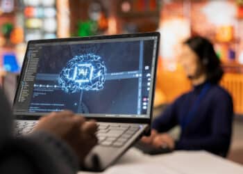 Tela de notebook exibe representação gráfica de um cérebro digital com a inscrição "AI", simbolizando o uso da inteligência artificial no ambiente corporativo.