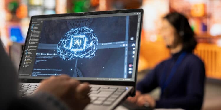 Tela de notebook exibe representação gráfica de um cérebro digital com a inscrição "AI", simbolizando o uso da inteligência artificial no ambiente corporativo.