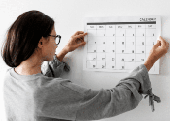 Pessoa de cabelos escuros fixando calendário mensal na parede branca