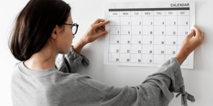 Pessoa de cabelos escuros fixando calendário mensal na parede branca