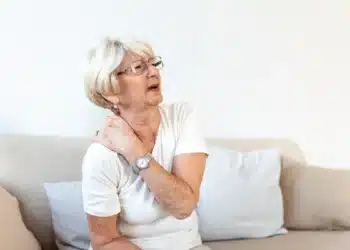 Mulher idosa sentindo dor no pescoço, refletindo a experiência de quem vive com fibromialgia, uma condição que o Ministério Público recomenda não ser classificada como deficiência.