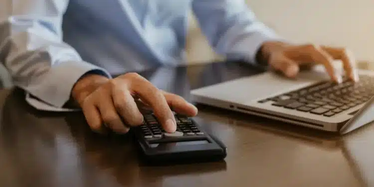 Pessoa utilizando calculadora e notebook para organizar valores do Imposto de Renda 2026 e registrar contribuições previdenciárias de dependentes.