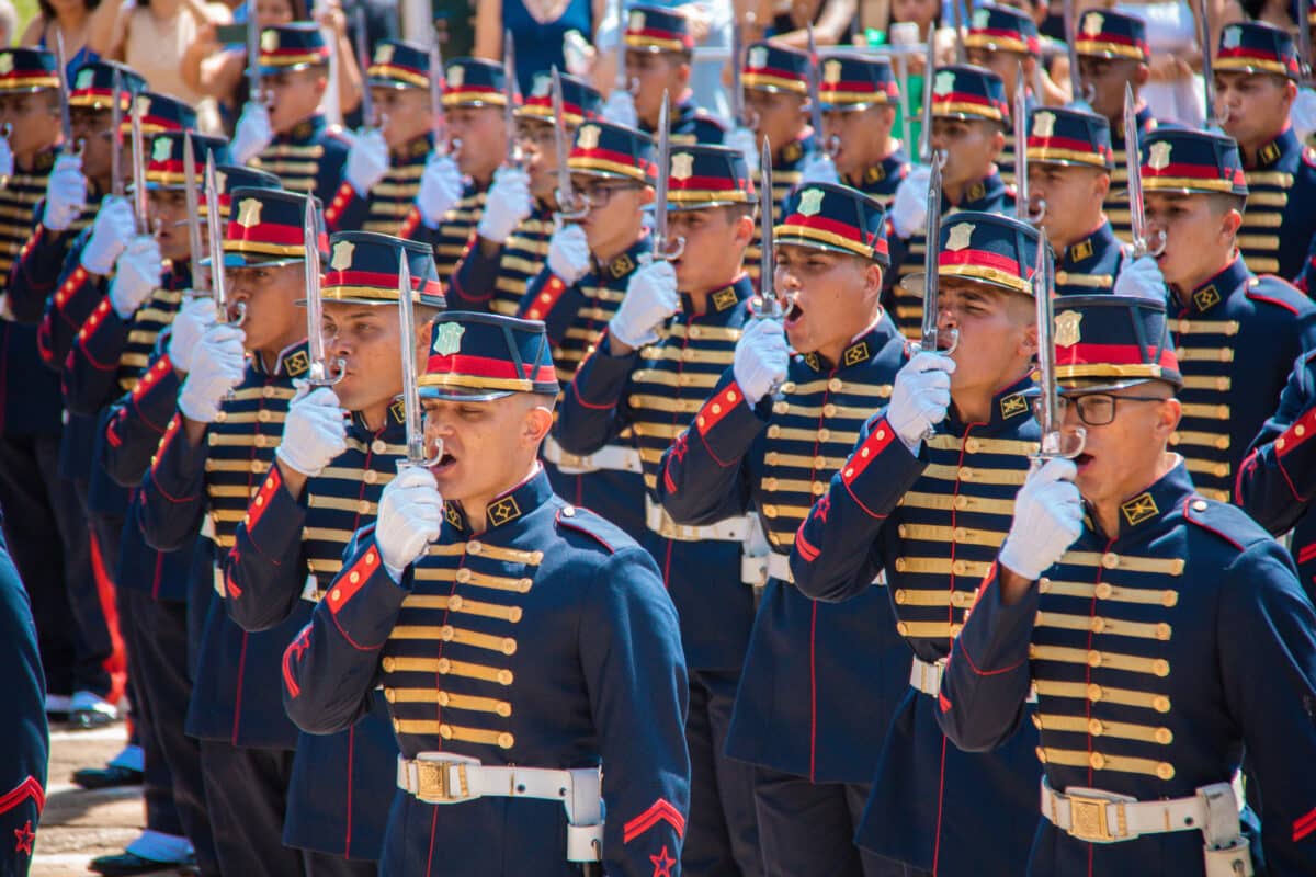 Cadetes do Exército Brasileiro desfilando em formação com uniformes azuis e detalhes dourados e vermelhos representando o concurso da ESA 2026