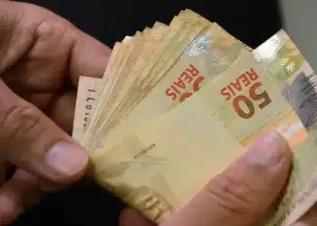 Notas de 50 reais sendo contadas, representando o pagamento do INSS com adicional de 50% em abril.