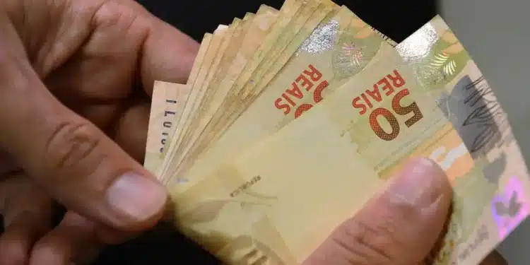 Notas de 50 reais sendo contadas, representando o pagamento do INSS com adicional de 50% em abril.