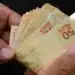 Notas de 50 reais sendo contadas, representando o pagamento do INSS com adicional de 50% em abril.