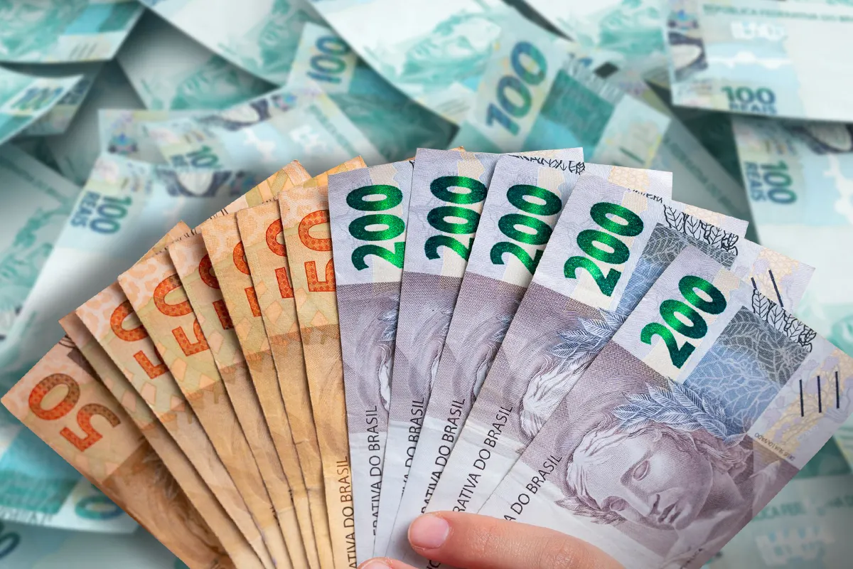 Notas de 50, 100 e 200 reais sendo exibidas, simbolizando os pagamentos do INSS e a 1ª parcela do 13º salário de abril.