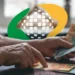 Aposentado recebendo pagamento do INSS em notas de R$ 100, R$ 50 e R$ 20, com o logo do INSS em fundo borrado.