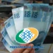 Nota de 100 reais em destaque, com a logomarca do INSS e empilhamento de cédulas de diferentes valores, ilustrando o pagamento de até R$ 8.475,55 para beneficiários com cartão final 3, 4, 5, 8, 9 e 0.