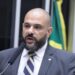 Deputado Sargento Portugal aparece com visual que adotou durante sua trajetória política: careca e barba. Enquanto esteve na Câmara dos Deputados, foi vice-líder do PSDB e vice-líder da Minoria. Veste terno cinza escuro com gravata listrada azul e branco, discursando ao microfone com bandeira brasileira desfocada ao fundo.