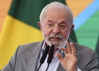 Presidente Lula discursando em evento com bandeira do Brasil ao fundo sobre proposta do Pé-de-Meia para universitários