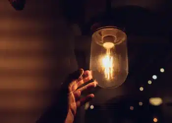 Mão alcançando lâmpada acesa, simbolizando o alerta sobre golpes digitais no programa Luz do Povo.