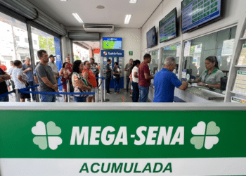 Fila de pessoas em casa lotérica aguardando para apostar na Mega-Sena acumulada, com painel verde destacado