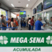 Fila de pessoas em casa lotérica aguardando para apostar na Mega-Sena acumulada, com painel verde destacado