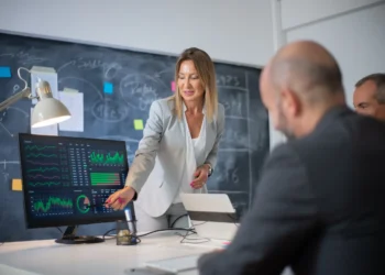 Profissional apresentando gráficos financeiros em tela para equipe durante reunião de estratégia no mercado financeiro.