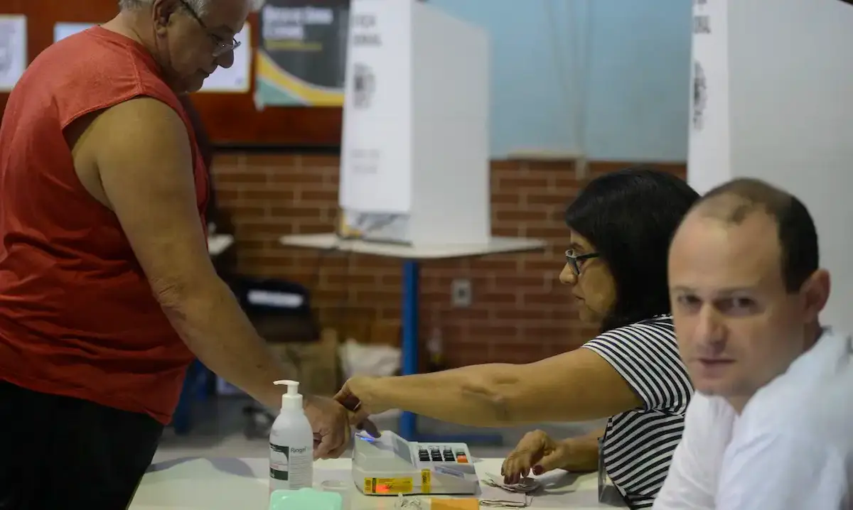 Mesários voluntários orientando eleitores no processo de votação durante as Eleições.