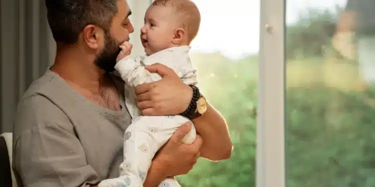 Pai segurando seu bebê em casa, com um sorriso de carinho, simbolizando as novidades da licença-paternidade