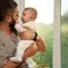 Pai segurando seu bebê em casa, com um sorriso de carinho, simbolizando as novidades da licença-paternidade