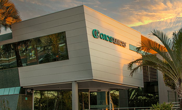 Fachada externa de unidade da Oncoclínicas com logotipo em destaque ao entardecer