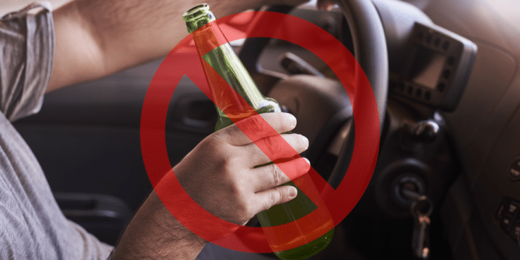 Mão masculina segura garrafa verde de cerveja atrás do volante com sinal vermelho de proibição sobreposto