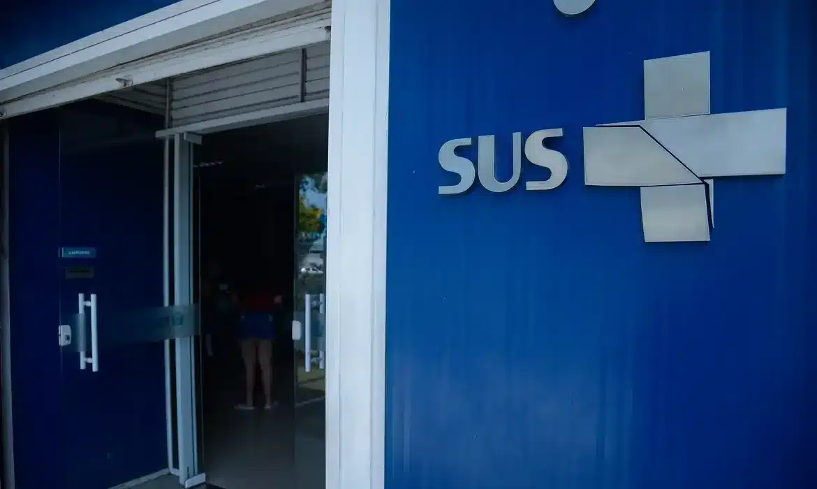 Fachada de unidade de saúde do SUS, destacando o logo e o ambiente, com pacientes acessando o atendimento médico.