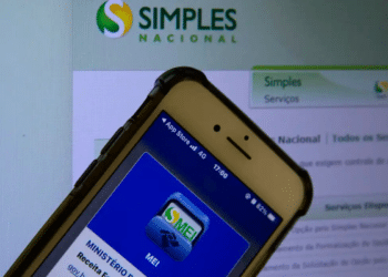 Smartphone com app MEI aberto na tela sobre monitor exibindo Portal do Simples Nacional