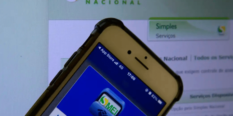 Smartphone com app MEI aberto na tela sobre monitor exibindo Portal do Simples Nacional