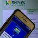 Smartphone com app MEI aberto na tela sobre monitor exibindo Portal do Simples Nacional