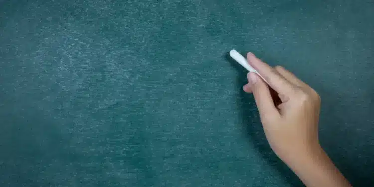 Uma mão escrevendo em um quadro-negro, simbolizando o direito dos professores temporários ao piso nacional, conforme decisão do STF.