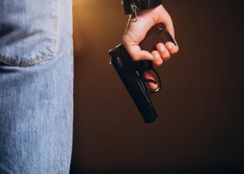 Pessoa segurando arma de fogo ao lado do corpo, representando profissões com autorização de porte no Brasil.