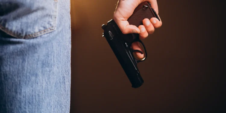Pessoa segurando arma de fogo ao lado do corpo, representando profissões com autorização de porte no Brasil.