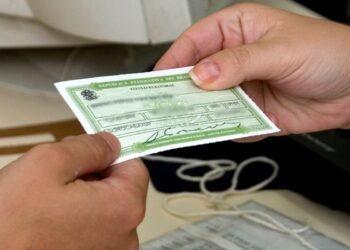 Pessoa segurando o título de eleitor brasileiro com informações visíveis no documento.