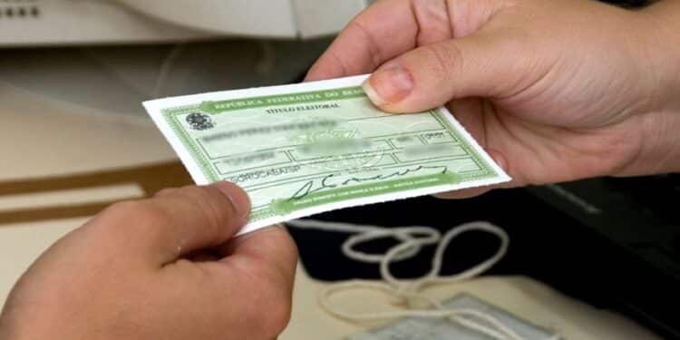 Pessoa segurando o título de eleitor brasileiro com informações visíveis no documento.