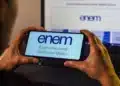 Pessoa segurando celular exibindo o logo do Enem, com o título 'Exame Nacional do Ensino Médio'.