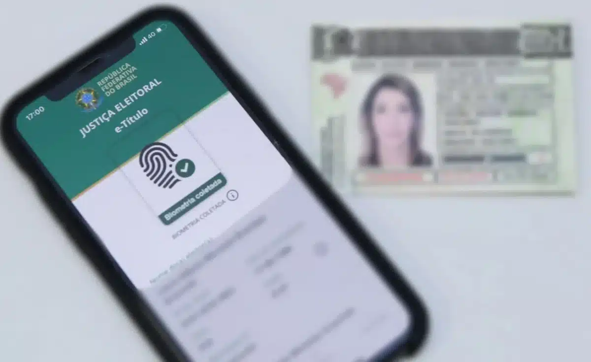 aplicativo e-Título da Justiça Eleitoral mostrando a biometria coletada, com um título de eleitor em segundo plano, simbolizando o processo de regularização eleitoral.