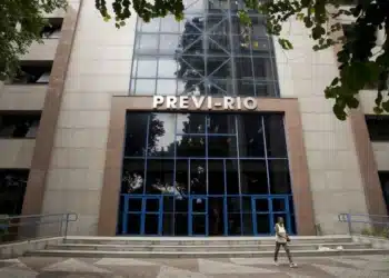 Fachada do prédio do Instituto de Previdência Previ-Rio, com um pedestre passando pela escada principal, alertando sobre a convocação para a Prova de Vida para aposentados e pensionistas.