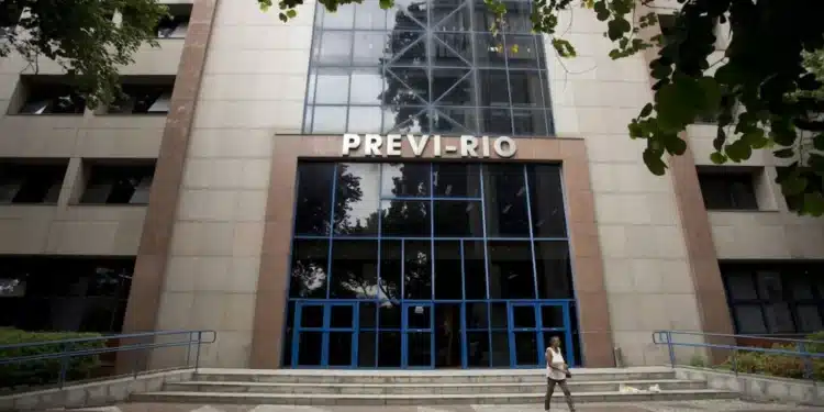 Fachada do prédio do Instituto de Previdência Previ-Rio, com um pedestre passando pela escada principal, alertando sobre a convocação para a Prova de Vida para aposentados e pensionistas.