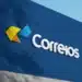 Letreiro 3D dos Correios em fachada azul com símbolo de setas amarela e azul e logotipo branco