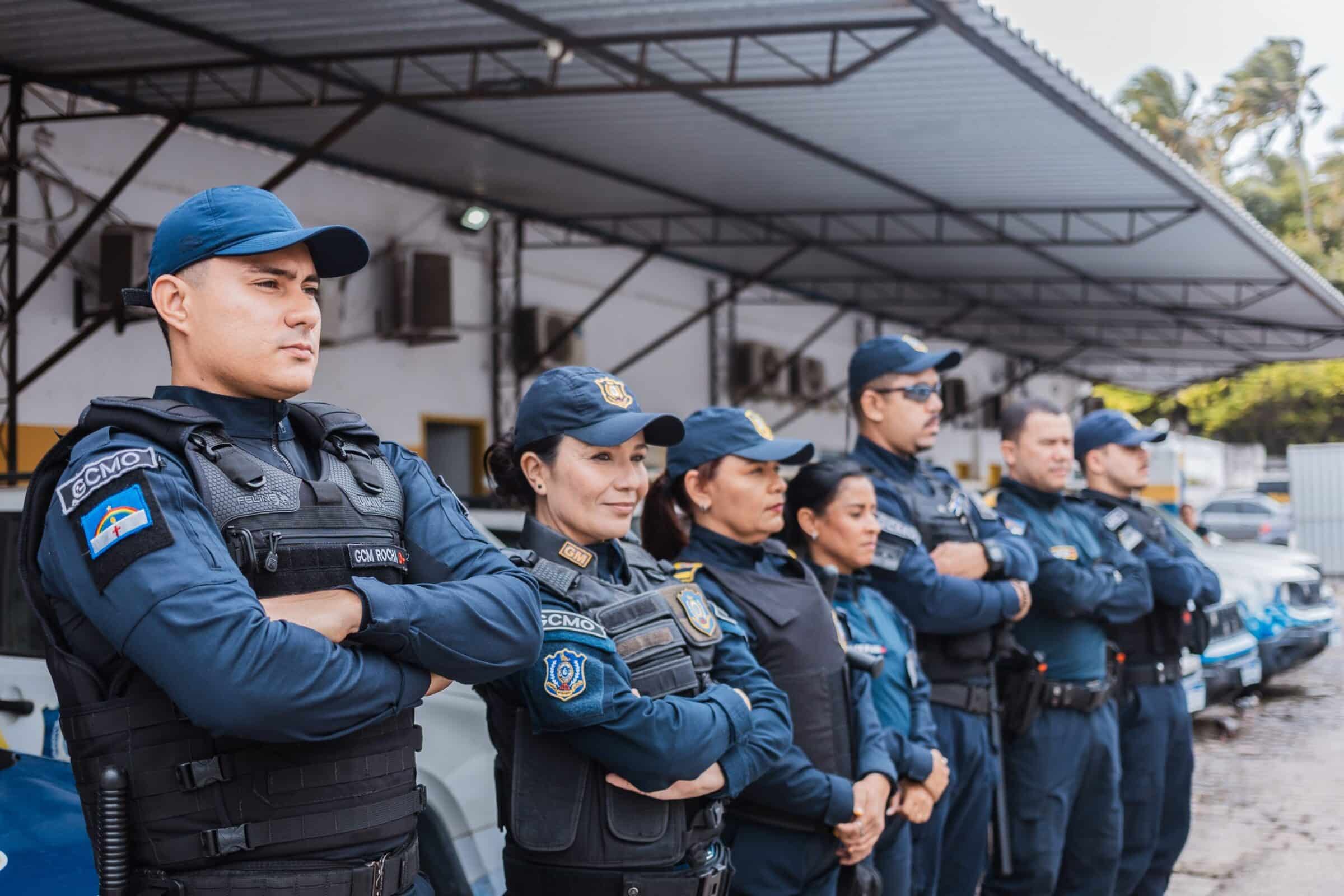 Nove agentes da GCMO de Olinda enfileirados com braços cruzados, usando uniformes azul marinho, coletes e bonés