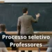 Professor escrevendo em quadro em sala de aula durante processo seletivo público.