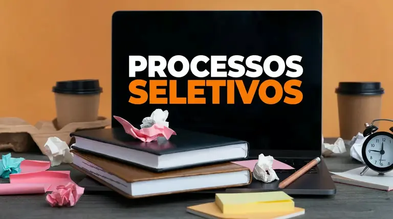 Imagem com livros, papéis amassados e um laptop, destacando a frase 'Processos Seletivos' em laranja, ilustrando os processos seletivos da Prefeitura de Brusque.