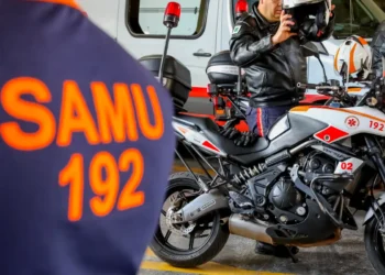 Profissional do SAMU em motolância equipada para atendimento pré-hospitalar , ao lado de uniforme laranja com inscrição SAMU 192.