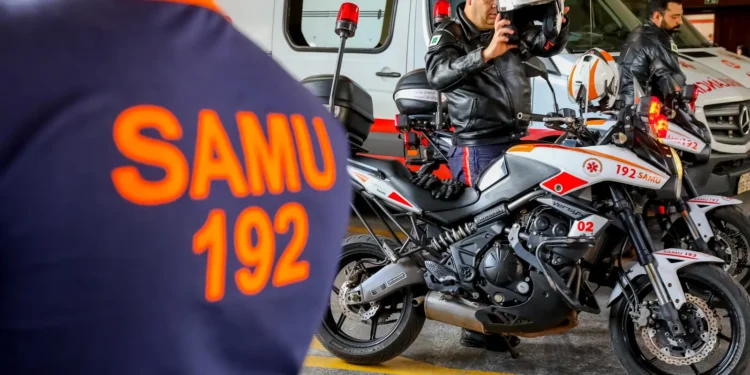 Profissional do SAMU em motolância equipada para atendimento pré-hospitalar , ao lado de uniforme laranja com inscrição SAMU 192.