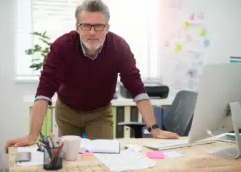 Profissional experiente com mais de 50 anos trabalhando em escritório moderno e demonstrando liderança no ambiente corporativo.