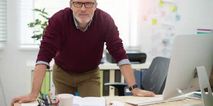 Profissional experiente com mais de 50 anos trabalhando em escritório moderno e demonstrando liderança no ambiente corporativo.