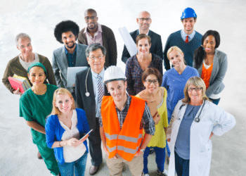 Grupo de 14 pessoas com roupas profissionais variadas, incluindo médicos, engenheiros, enfermeiros e executivos, olhando para cima e sorrindo