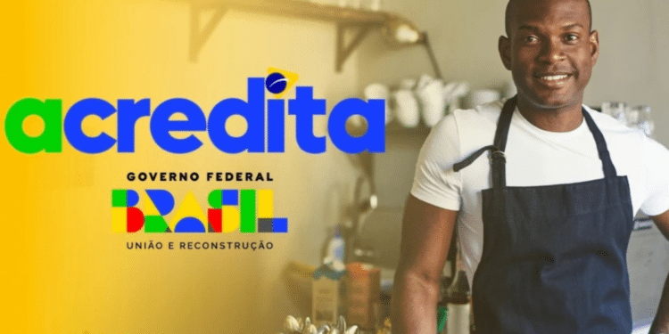 Homem negro sorridente usa avental azul-marinho em cozinha profissional, ao lado da marca do Programa Acredita