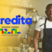 Homem negro sorridente usa avental azul-marinho em cozinha profissional, ao lado da marca do Programa Acredita