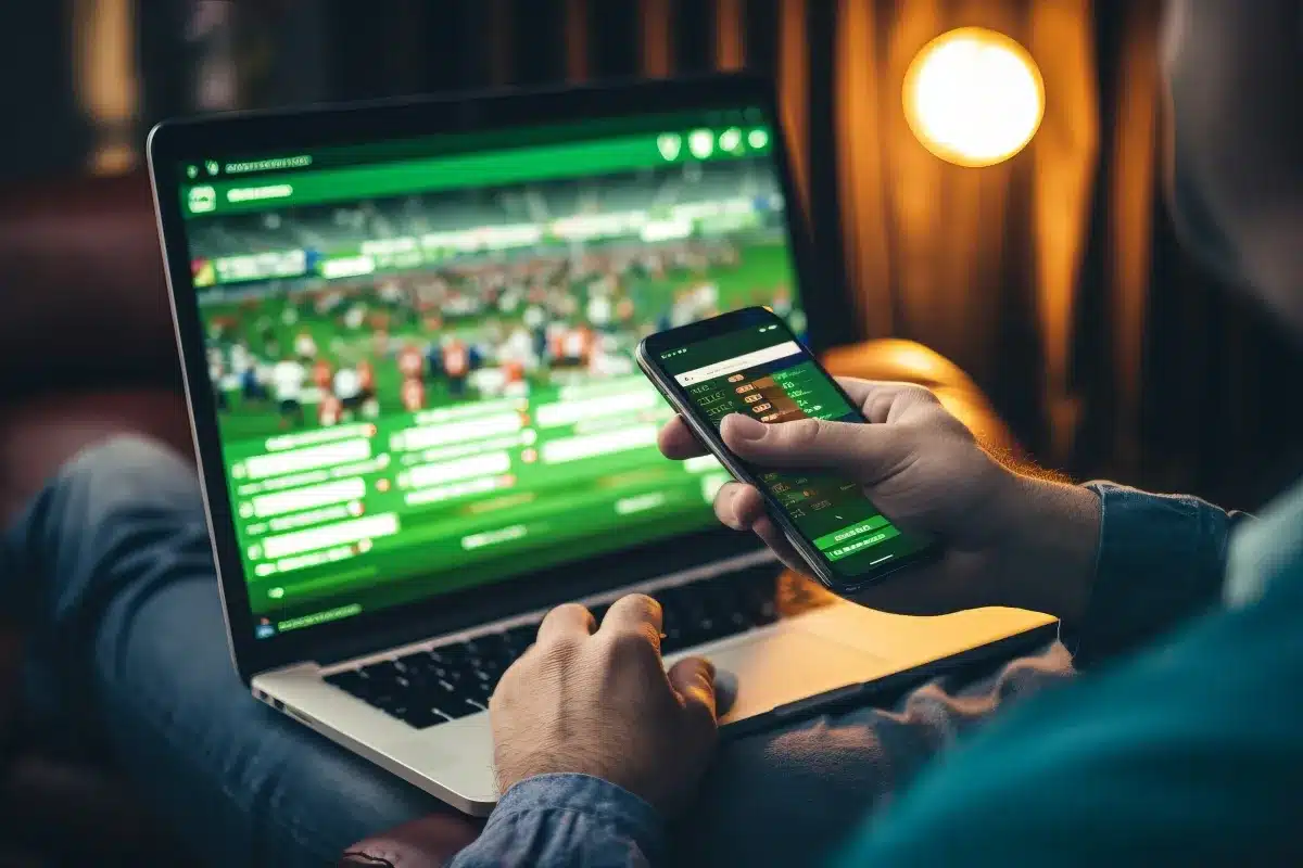 Pessoa acessando apostas online em um laptop e smartphone, com foco em jogos esportivos, que serão proibidos a partir de maio.